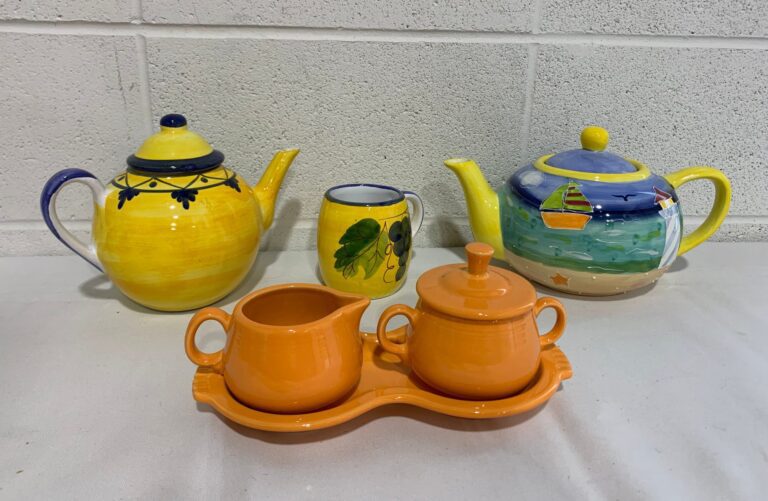 2 colorful teapots, one mug, one orange cream and sugar set