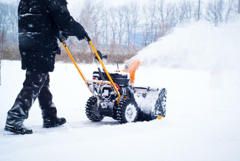 A person pushes a snowblower to clear a driveway