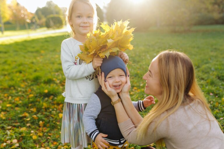 Happy family, a mom with 2 children in the park playing with leaves