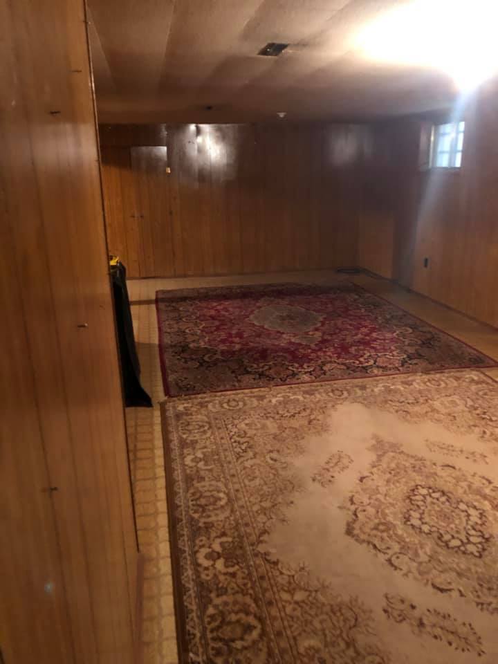 A basement in a home with 2 rugs on the floor, with wooden walls