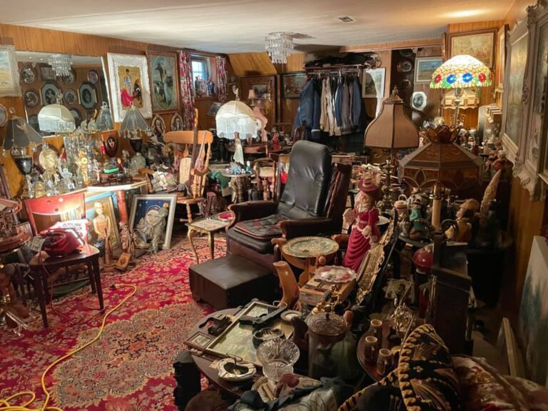 A living room with wooden walls packed with old fashioned items and furniture, leaving almost no room to move around.