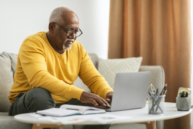 Senior Black Man Typing On Laptop Working Online Indoor