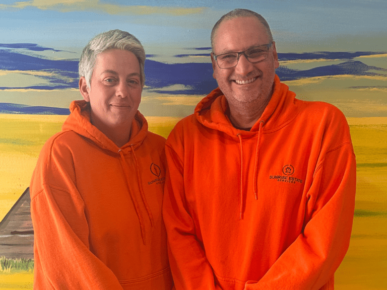 Sunrise Estate Services staff stand in front of a sunrise mural wearing orange hoodies